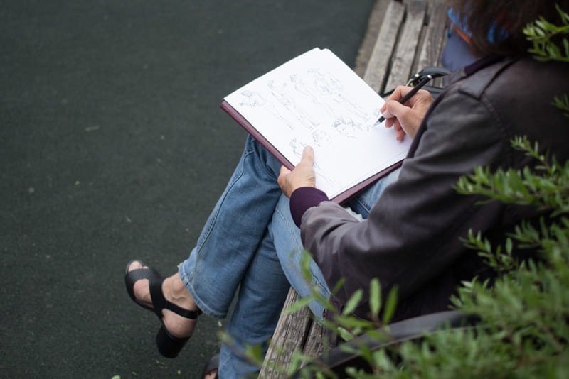 Mulher sentada em branco na rua rabiscando em sketchbook