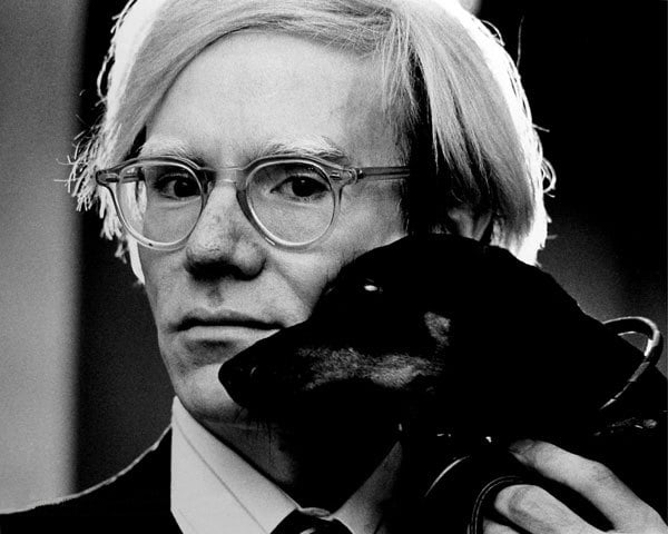 Foto de Andy Warhol segurando um cachorro próximo ao rosto